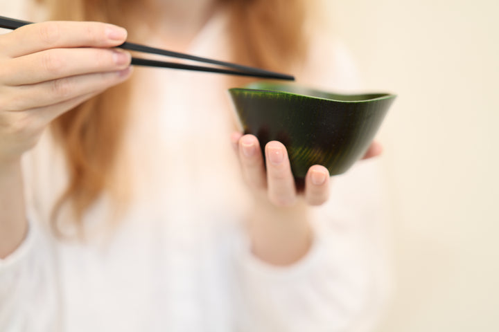 Close view of an adult model supporting the RIN Bowl M Olive with chopsticks above it.