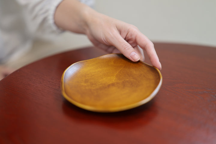 A hand reaching toward the RIN 5.0 Mimosa plate on a warm reddish-brown tabletop.