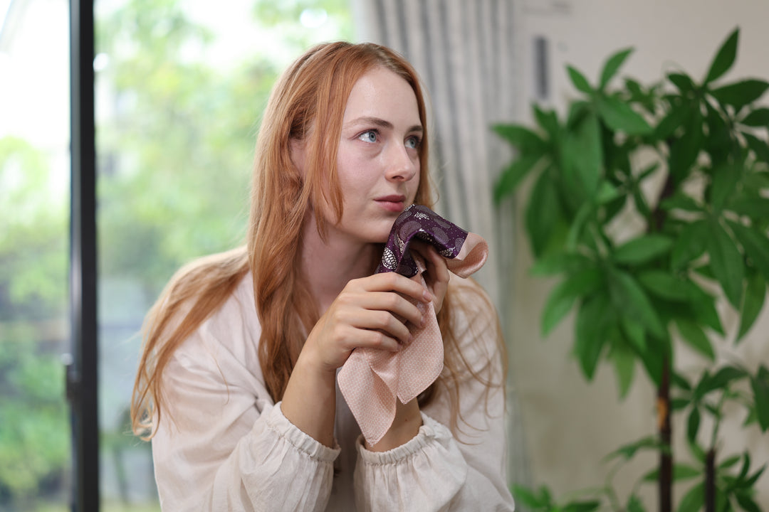 Purple-and-pink silk pocket square loosely gathered in a person's hands by a window.
