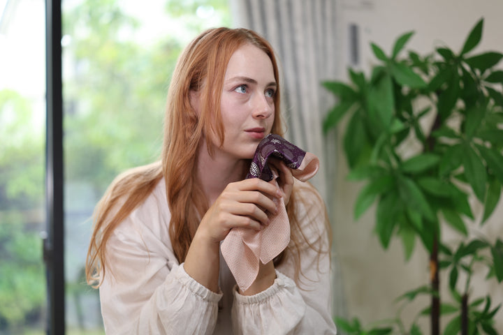 Purple-and-pink silk pocket square loosely gathered in a person's hands by a window.