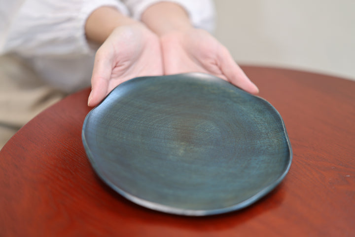 Hands presenting the low rim and irregular outline of the RIN 7.0 Hyacinth on a red table.