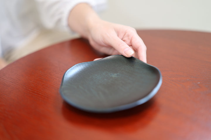 A hand holding the edge of the dark lacquered RIN 5.0 Hyacinth plate on a red wooden table.