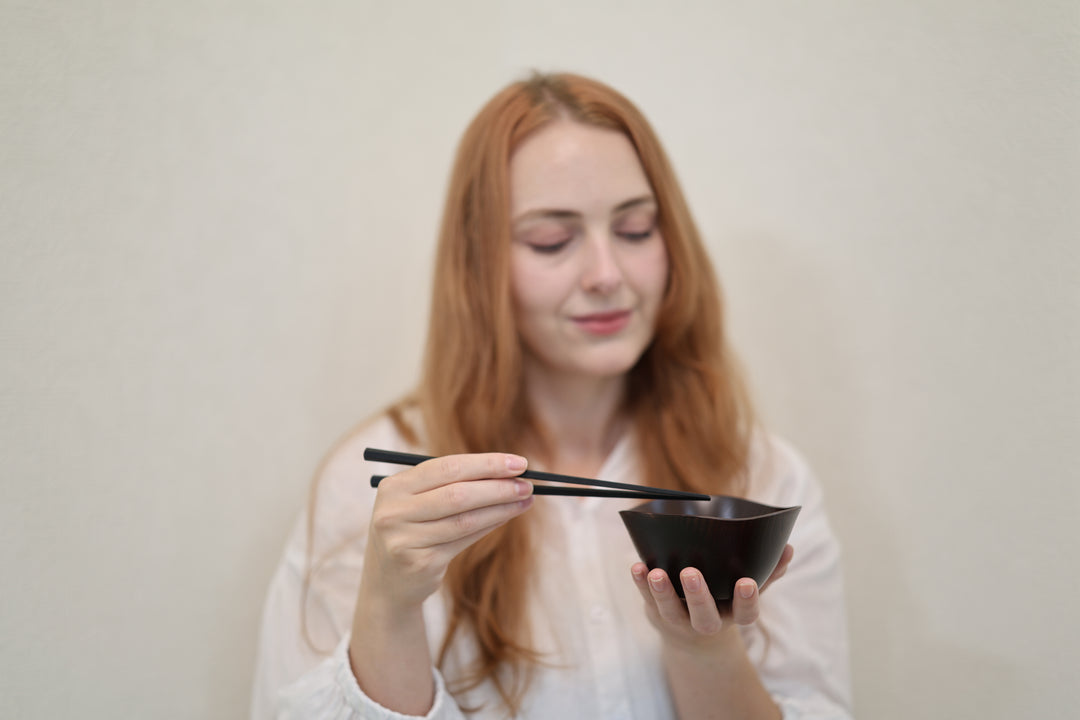 Adult model holding the RIN Bowl M Lilac and chopsticks against a softly focused pale wall.