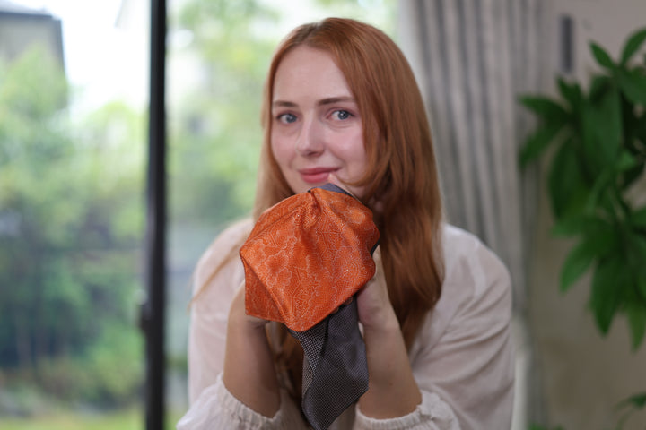 Front-facing portrait with the model holding the patterned silk square close to the camera.