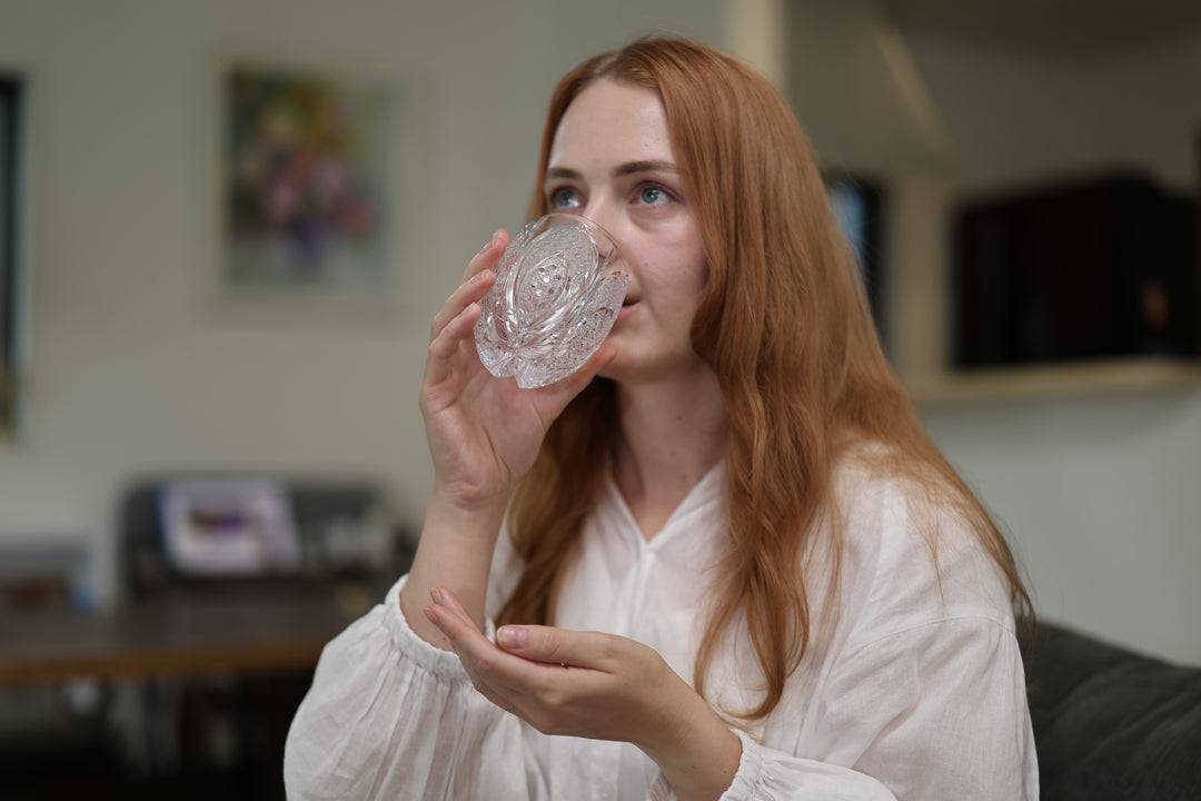 Adult model taking a sip from SHIROHANA: Clear while seated in a softly lit room.