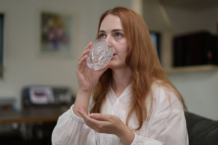 Adult model taking a sip from SHIROHANA: Clear while seated in a softly lit room.