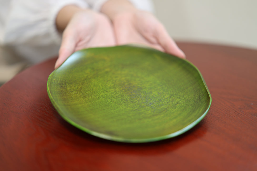 A hand approaching the low irregular rim of the RIN 7.0 Olive on a red table.