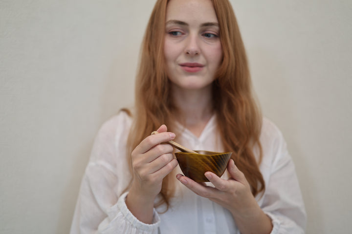 Adult model holding the small RIN Bowl S Mimosa with a wooden spoon against a plain indoor wall.