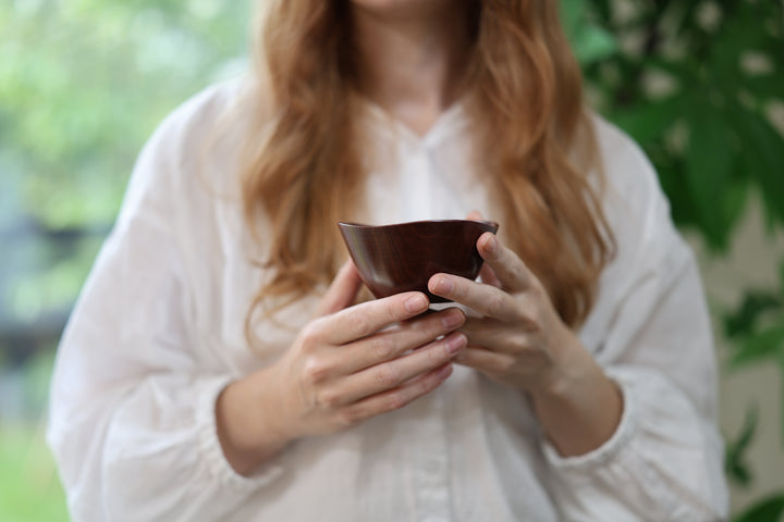 An adult model holding the empty RIN Bowl S Berry against a softly lit interior with greenery beyond.
