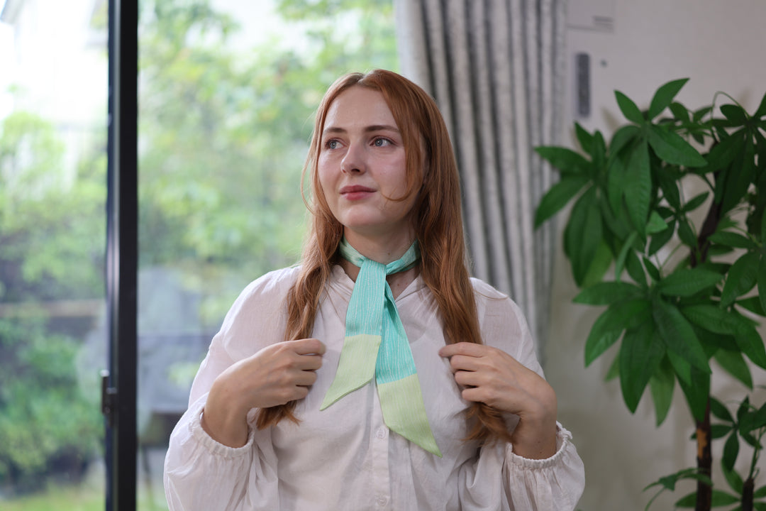 The green bamboo-pattern silk scarf tied at the neck over a white shirt.