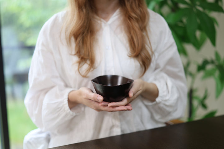 Adult model presenting the empty RIN Bowl M Lilac in both hands near a window.