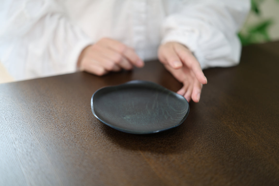 Hands framing the RIN 5.0 Hyacinth plate on a dark wooden table, with its grain and organic rim visible.