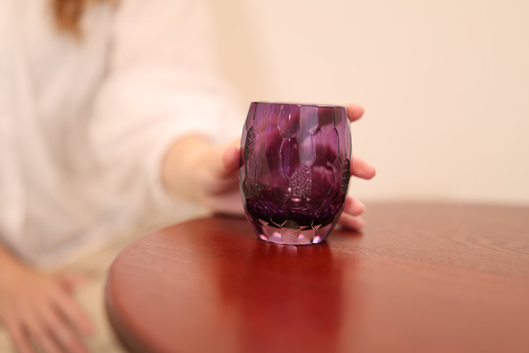 The purple Edo Kiriko glass on a wooden table with a seated person nearby.