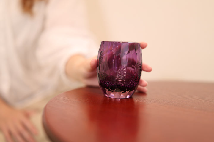 The purple Edo Kiriko glass on a wooden table with a seated person nearby.