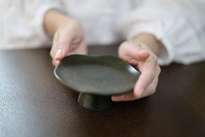 Two hands gently repositioning Floating Leaf Sesame, showing its shallow dish and raised pedestal.