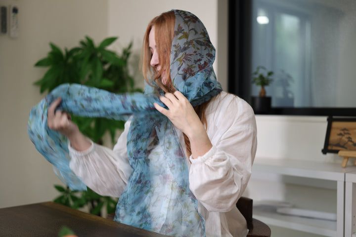 A wearer adjusting one end of the blue silk stole while it is gathered at the neck.