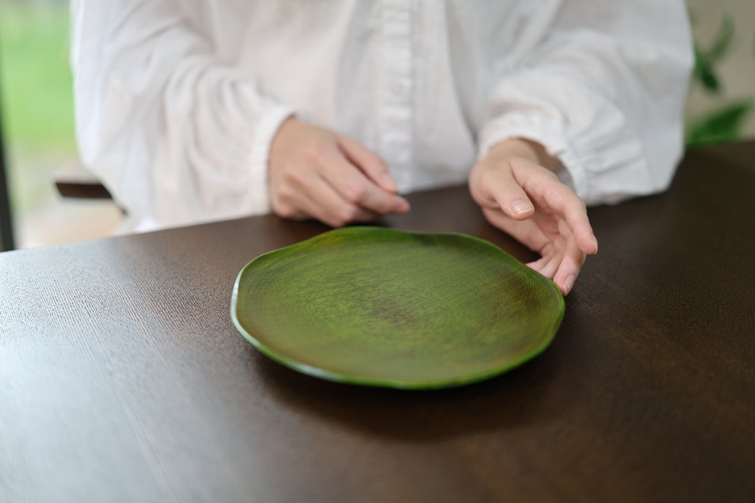Two hands framing the empty RIN 7.0 Olive on a dark tabletop while its center remains visible.