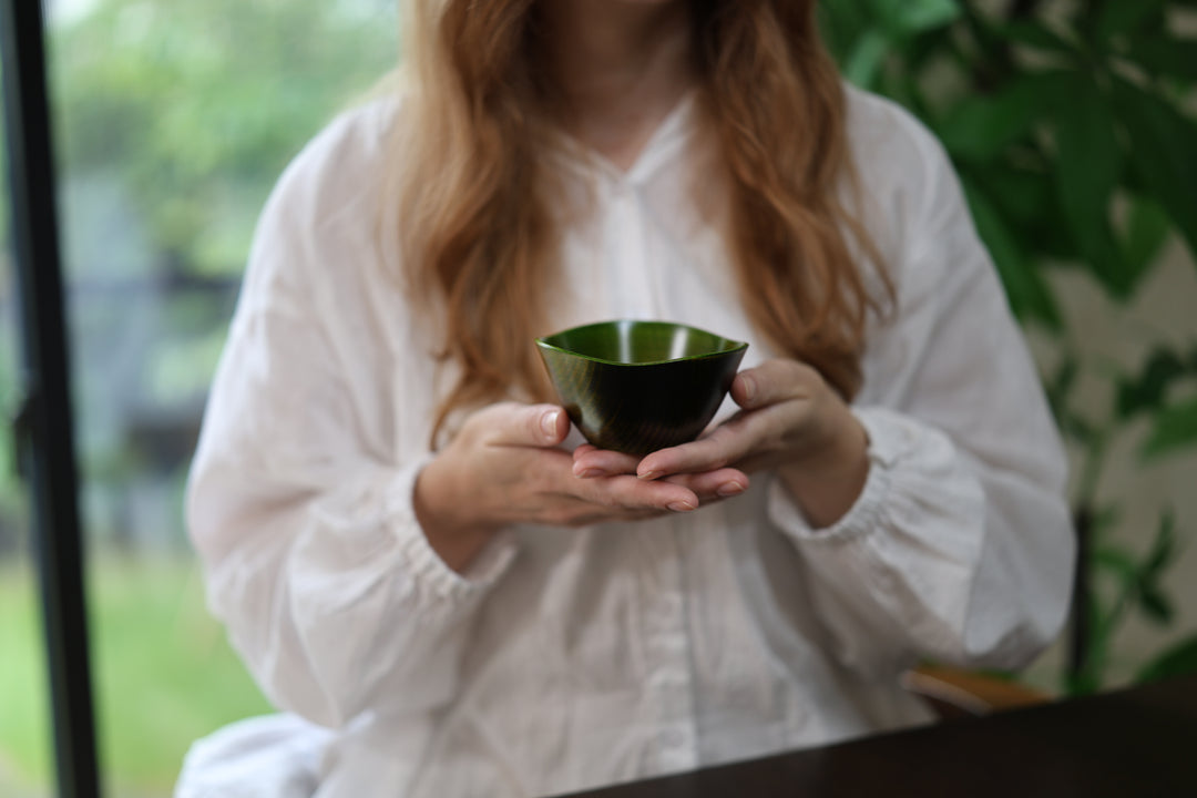 Adult model presenting the empty RIN Bowl S Olive in both hands in a softly lit interior.