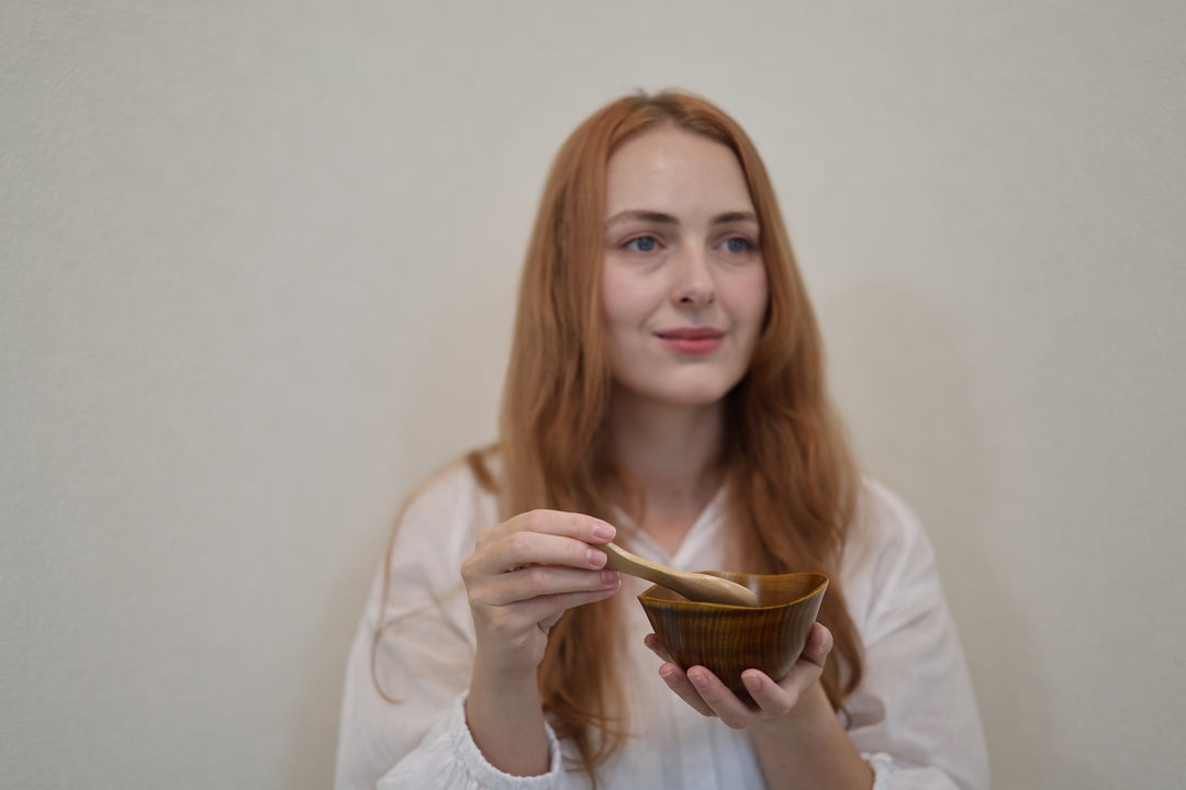 Adult model pausing with the empty RIN Bowl M Mimosa and a wooden spoon in a calm interior setting.