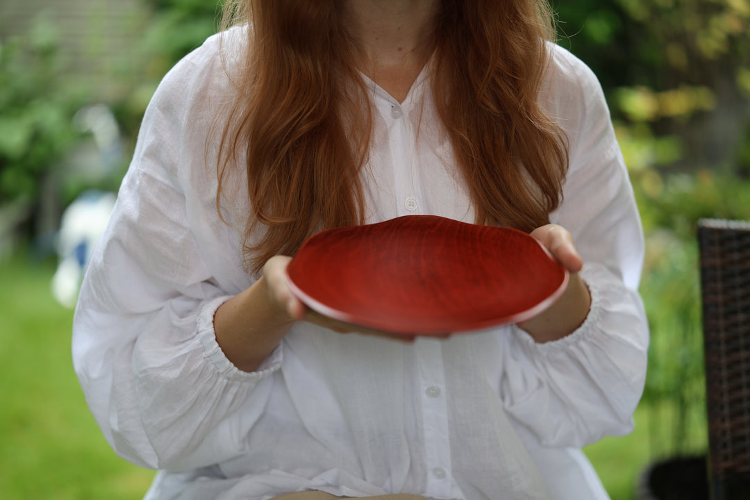 A person holding the berry-red RIN plate in a shaded outdoor setting