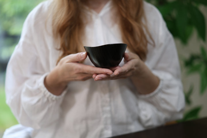 Adult model holding the empty RIN Bowl S Sesame in both hands near a window, with its rising rim visible.