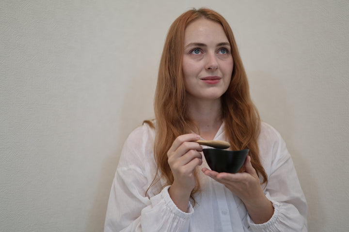 Adult model holding the RIN Bowl S Hyacinth with a wooden spoon in a wider interior portrait.