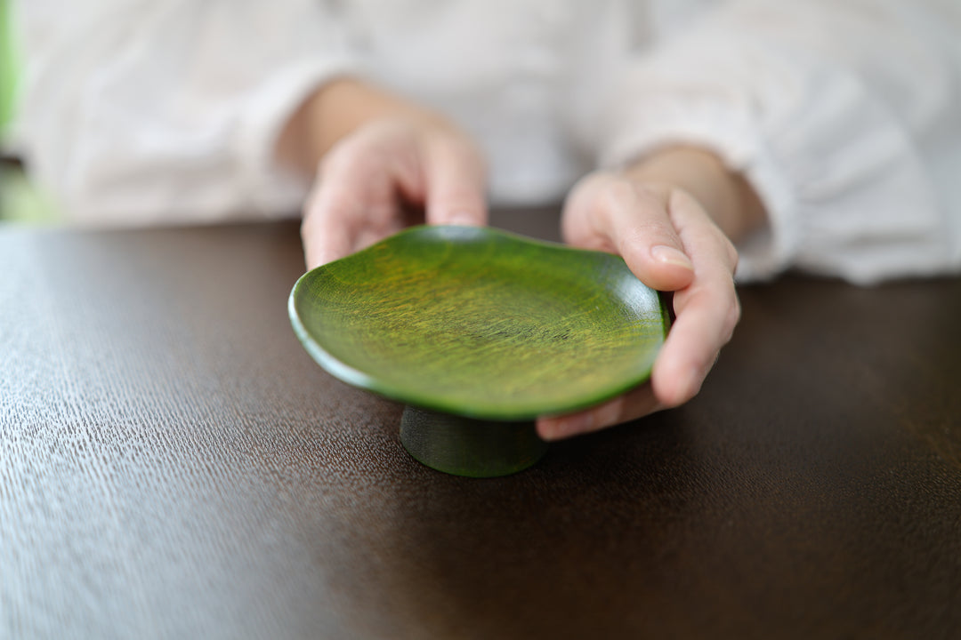 A close view of an adult gently holding the olive Floating Leaf lacquerware piece