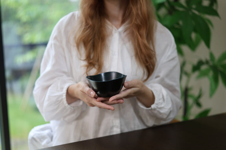 Adult model holding the empty RIN Bowl M Sesame in both hands near a window, with its rising rim visible.