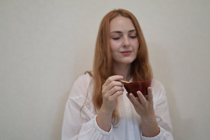 A wider indoor view of an adult model holding the RIN Bowl S Berry and a wooden spoon.