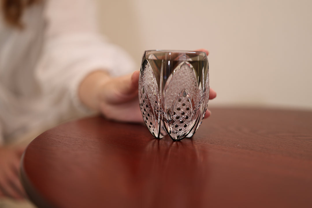 The Korohana Edo Kiriko vessel standing on a reddish wooden tabletop with a hand nearby.