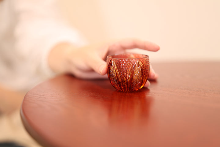 GENEN Gold-Red and Amber Edo Kiriko glass on a low table beside the hand of an adult model.
