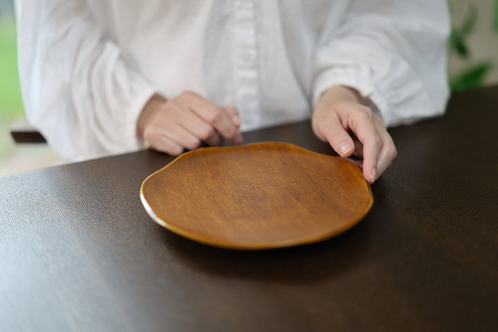 Adult model reaching toward the rim of an empty RIN 7.0 Mimosa plate on a dark table.