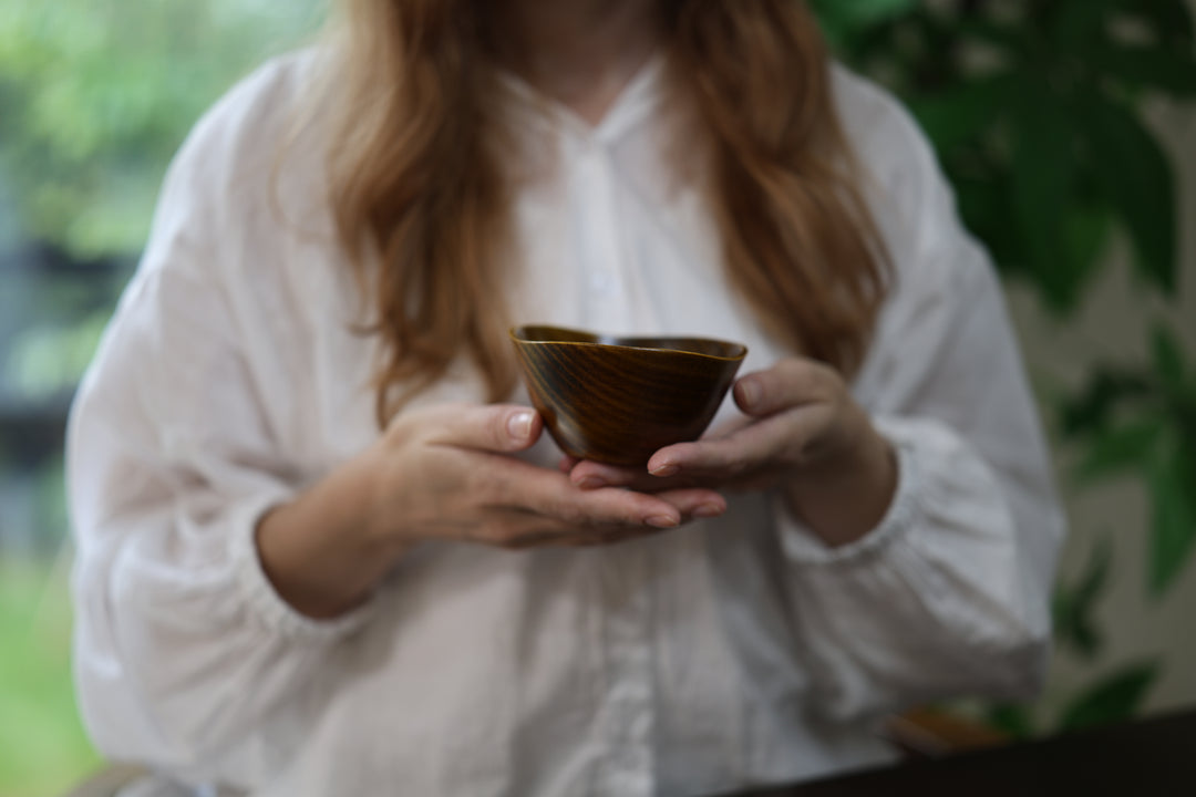 Adult model holding the empty RIN Bowl S Mimosa in both hands beside a softly lit window and greenery.