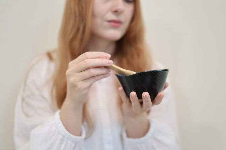 Adult model holding the empty RIN Bowl M Hyacinth at chest height with its irregular rim visible.