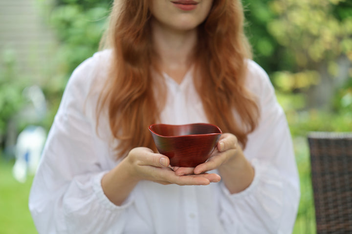 Adult model holding the RIN Bowl M Berry in both hands outdoors in soft shade.