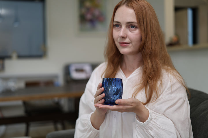 Seated woman holding the indigo Edo Kiriko glass in a quiet modern interior