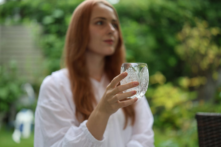 Adult model holding SHIROHANA: Clear upright in a garden setting with greenery behind it.