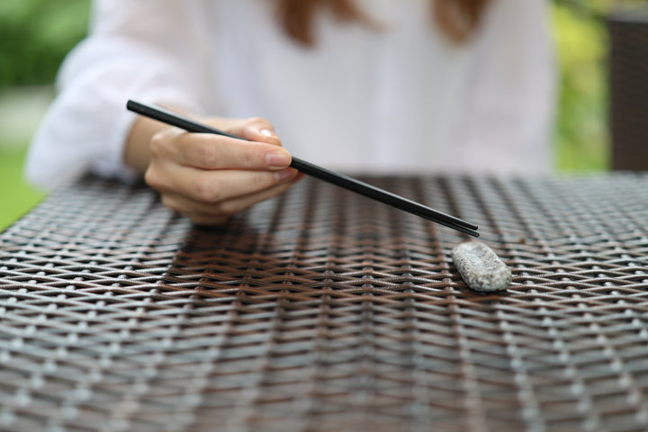 Makabe Stone Cutlery Rest and black chopsticks on an outdoor woven table in daylight.