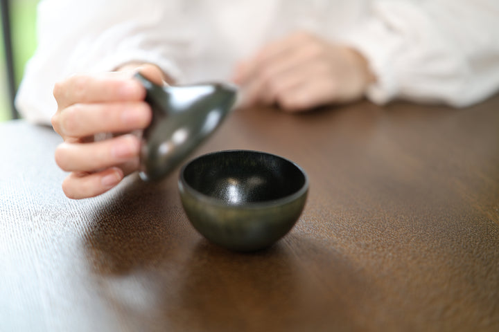 The lid of Bulb: Sesame lifted toward the foreground with the open base on a table.