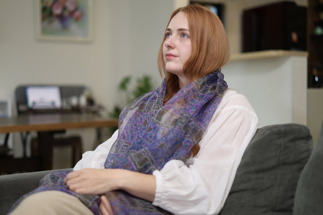 A wearer seated in a living room with the purple silk stole wrapped loosely at the neck.