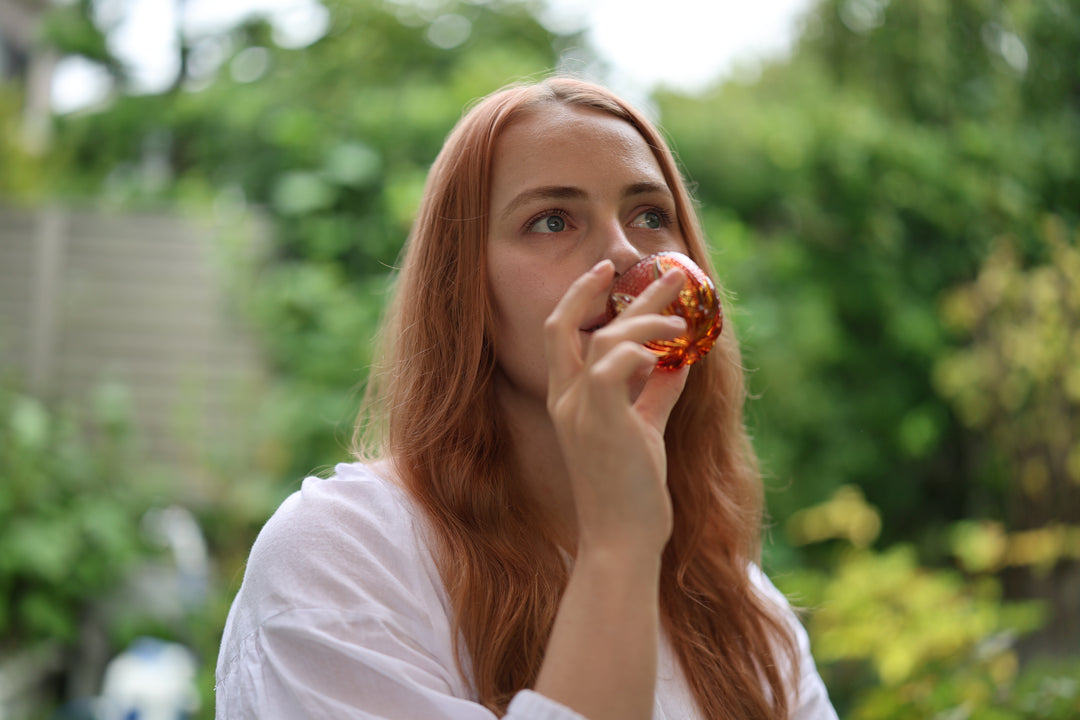 Adult model holding the GENEN Gold-Red and Amber Edo Kiriko glass in a garden setting.