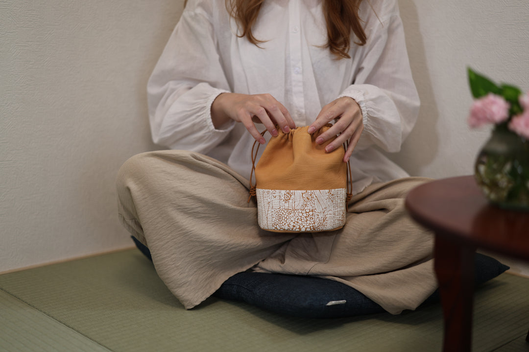 Natural leather drawstring pouch held by a seated person in a Japanese-style room.