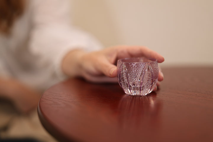 GENEN Gold-Purple Edo Kiriko glass on a low table beside the hand of an adult model.