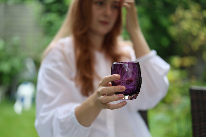 A person holding the purple cut-glass vessel in a green garden setting.