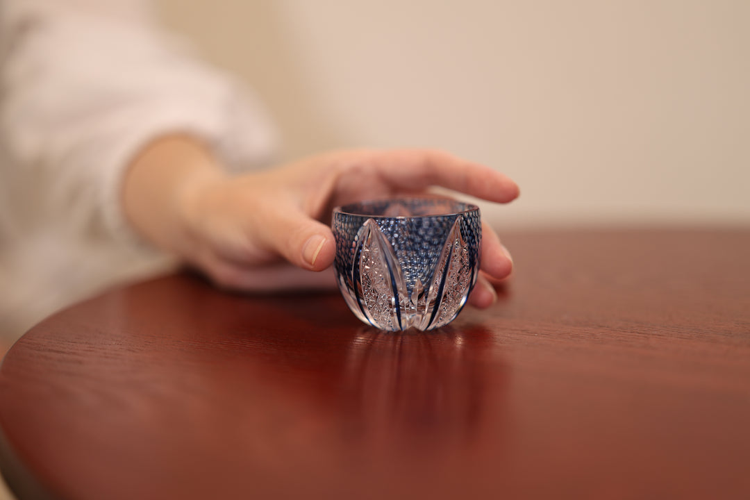 GENEN Indigo cut-glass vessel on a wooden table with an adult hand beside it.
