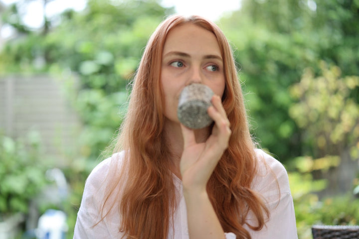 The Makabe stone cup raised for drinking in a green outdoor setting.