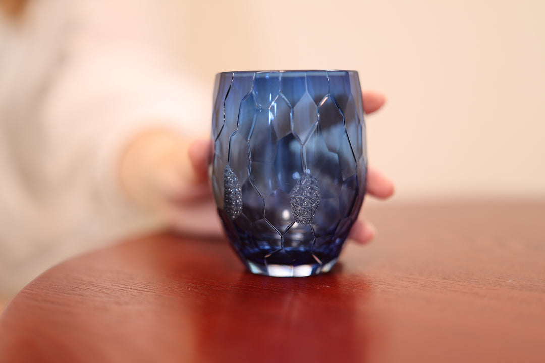 Indigo Edo Kiriko glass standing on a wooden table with a softly blurred person behind