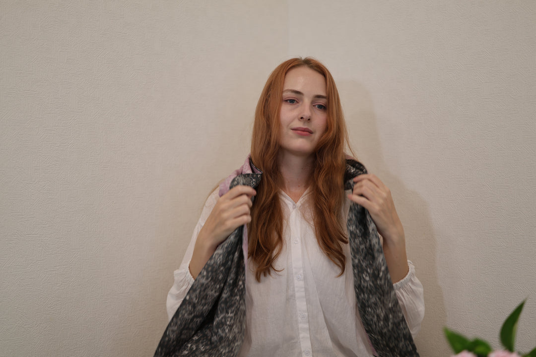 Model holding both ends of the purple and black reversible sumo-pattern stole indoors